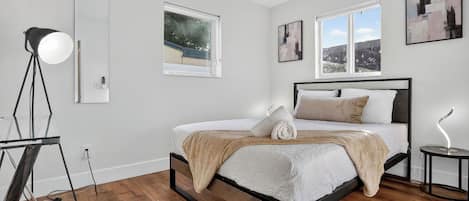 A modern bedroom with a bed, a standing lamp, and a window with a view.