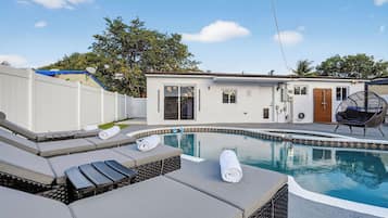 A swimming pool with lounge chairs and a small building with a door and windows.