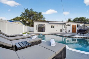 Ein Schwimmbecken mit Liegestühlen und ein kleines Gebäude mit Tür und Fenstern.