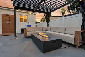 Ein moderner Außenbereich mit Feuerstelle, überdachter Sitzgelegenheit und Terrasse.