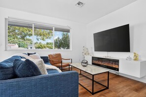 Ein modernes Wohnzimmer mit Sofa, Couchtisch, Kamin und einem an der Wand befestigten Fernseher.