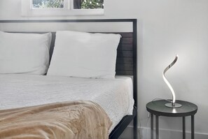 Ein Bett mit weißer Bettwäsche, einem hölzernen Kopfteil und einem Nachttisch mit moderner Lampe.