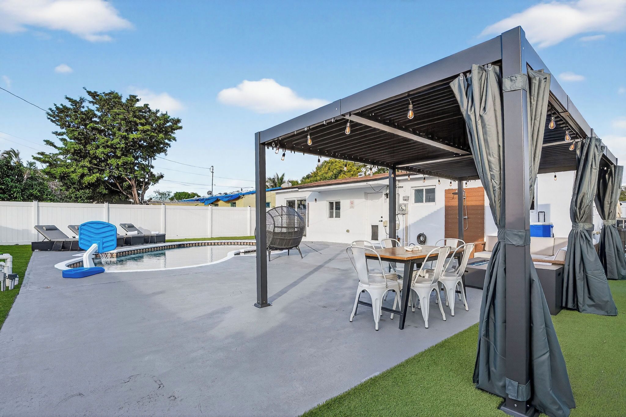 A covered outdoor patio with a pool, seating, and a pergola with hanging lights.