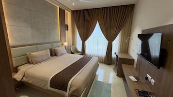 A hotel room with a large bed, a TV, a desk, and a view of the city through the window.