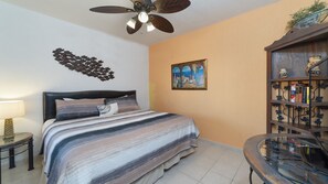 A bedroom with a bed, a ceiling fan, a wall art piece, a bookshelf, and a small table. - Sonoran Spa E-408 – Inviting Oceanview Condo with Relaxing Coastal Vibes (Puerto Peñasco)