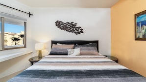 A bedroom with a bed, a wall-mounted artwork, a window with a view, and a nightstand with a lamp. - Sonoran Spa E-408 – Inviting Oceanview Condo with Relaxing Coastal Vibes (Puerto Peñasco)