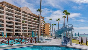A hotel with a pool area, including a water slide and lounge chairs. - Sonoran Spa E-408 – Inviting Oceanview Condo with Relaxing Coastal Vibes (Puerto Peñasco)