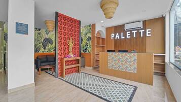 A modern interior with a reception desk labeled 'PALETTE,' a decorative wall with a geometric pattern, and a reception area with a patterned rug.