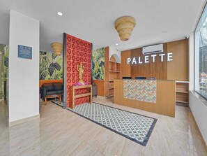 Un interior moderno con un mostrador de recepción con la etiqueta 'PALETTE', una pared decorativa con un diseño geométrico y un área de recepción con un alfombra estampado.