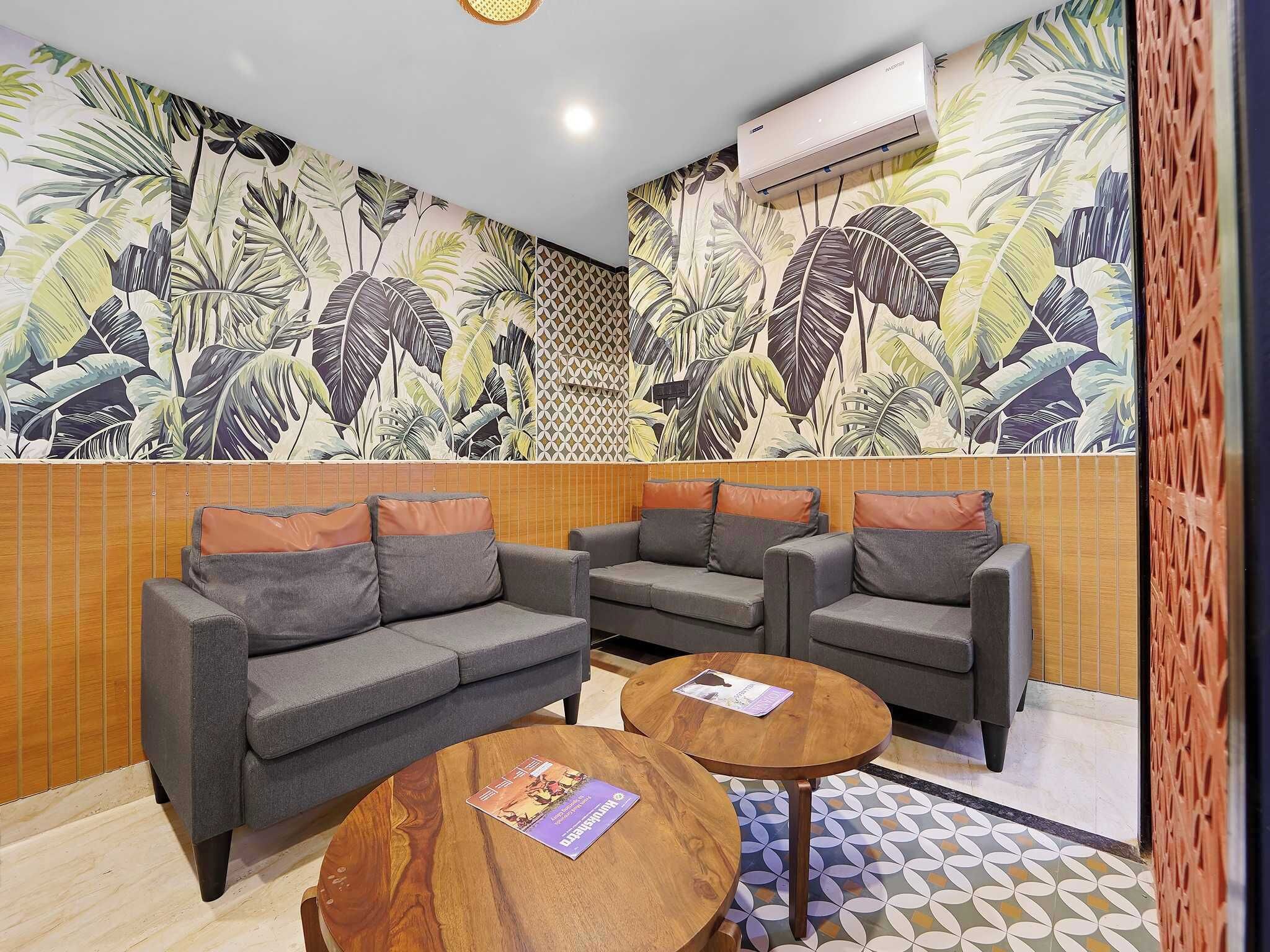 Una habitación con un conjunto de sofás, dos mesas de madera y un papel tapiz con motivos de hojas tropicales.