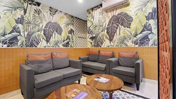Una habitación con un conjunto de sofás, dos mesas de madera y un papel tapiz con motivos de hojas tropicales.