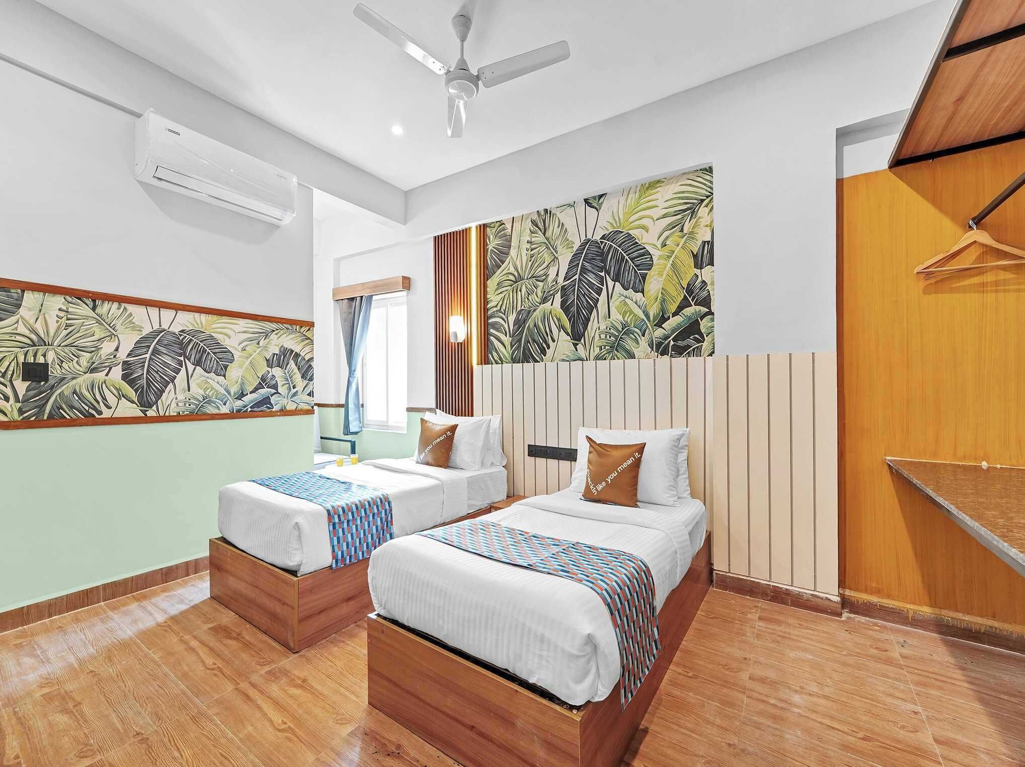 A hotel room with two beds, a ceiling fan, a large tropical leaf mural, and a wooden floor.