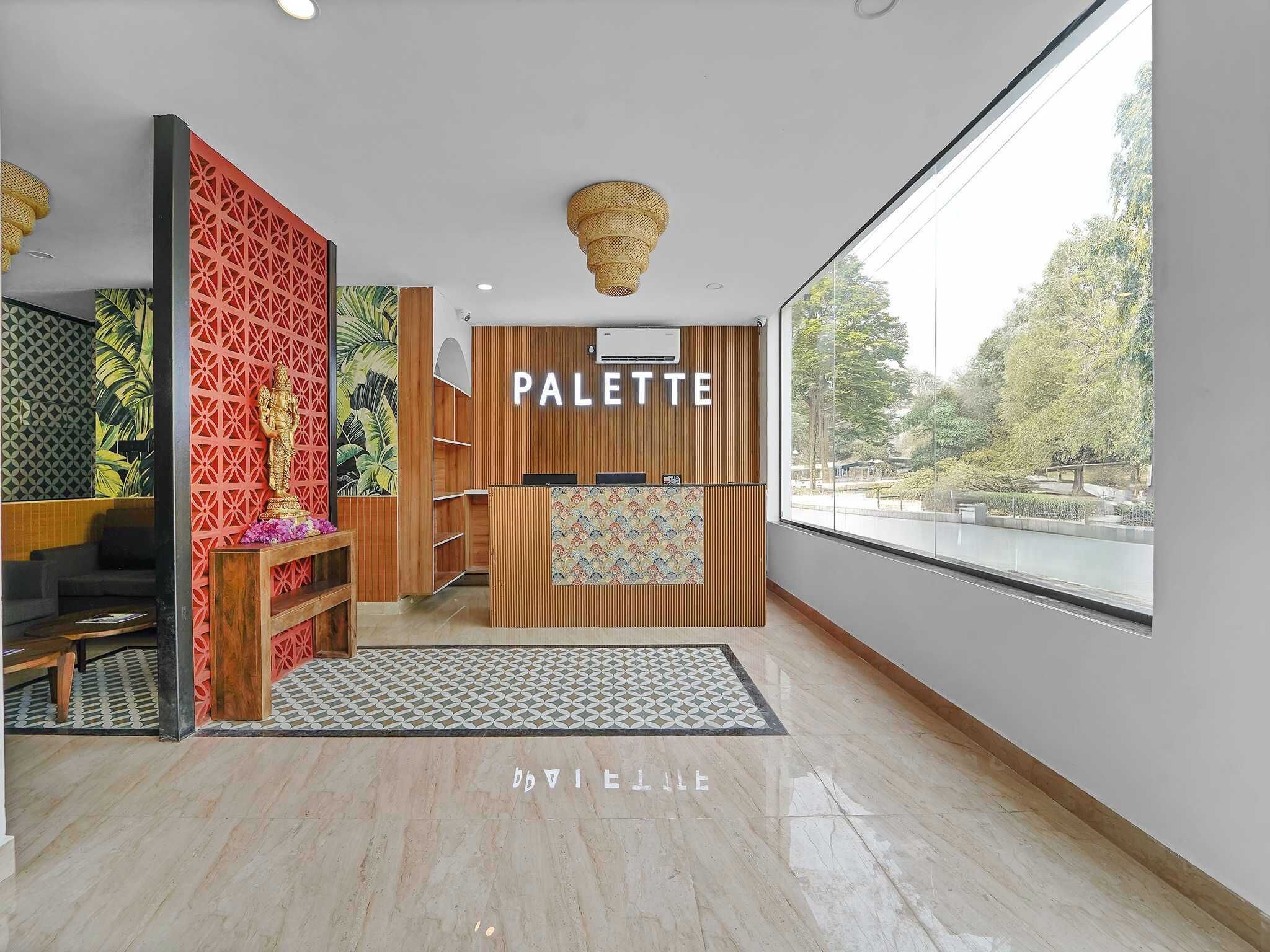 A reception area with a 'PALETTE' sign, a reception desk, a patterned wall, a statue, and a view through a large window.