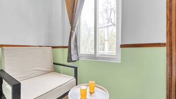 A room with a sofa, a small round table with two glasses of orange juice, and a window with a curtain.