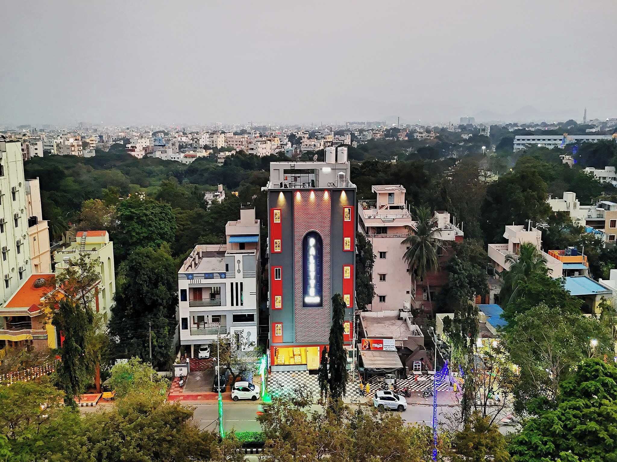 A multi-story building with a prominent central feature, surrounded by residential buildings and greenery.