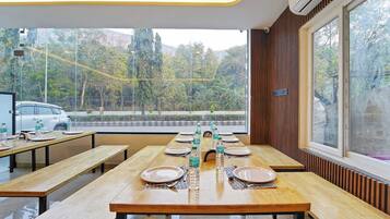 A dining area with wooden tables and benches, a view of trees and a road outside, and an air conditioning unit on the wall.