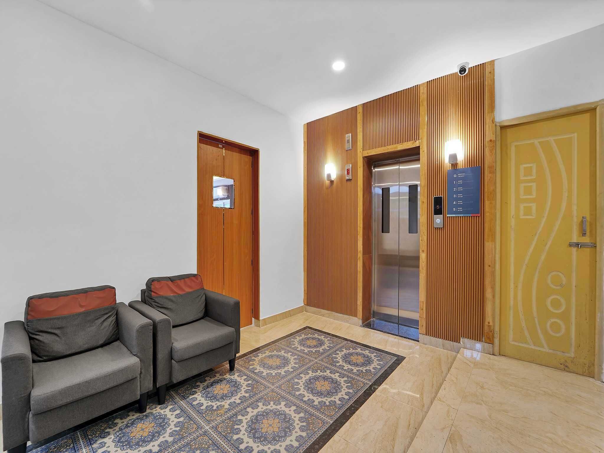 Un vestíbulo con mostrador de recepción, dos sofás, un tapete estampado, un ascensor y un panel de pared de madera.