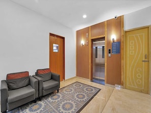 Un vestíbulo con mostrador de recepción, dos sofás, un tapete estampado, un ascensor y un panel de pared de madera.