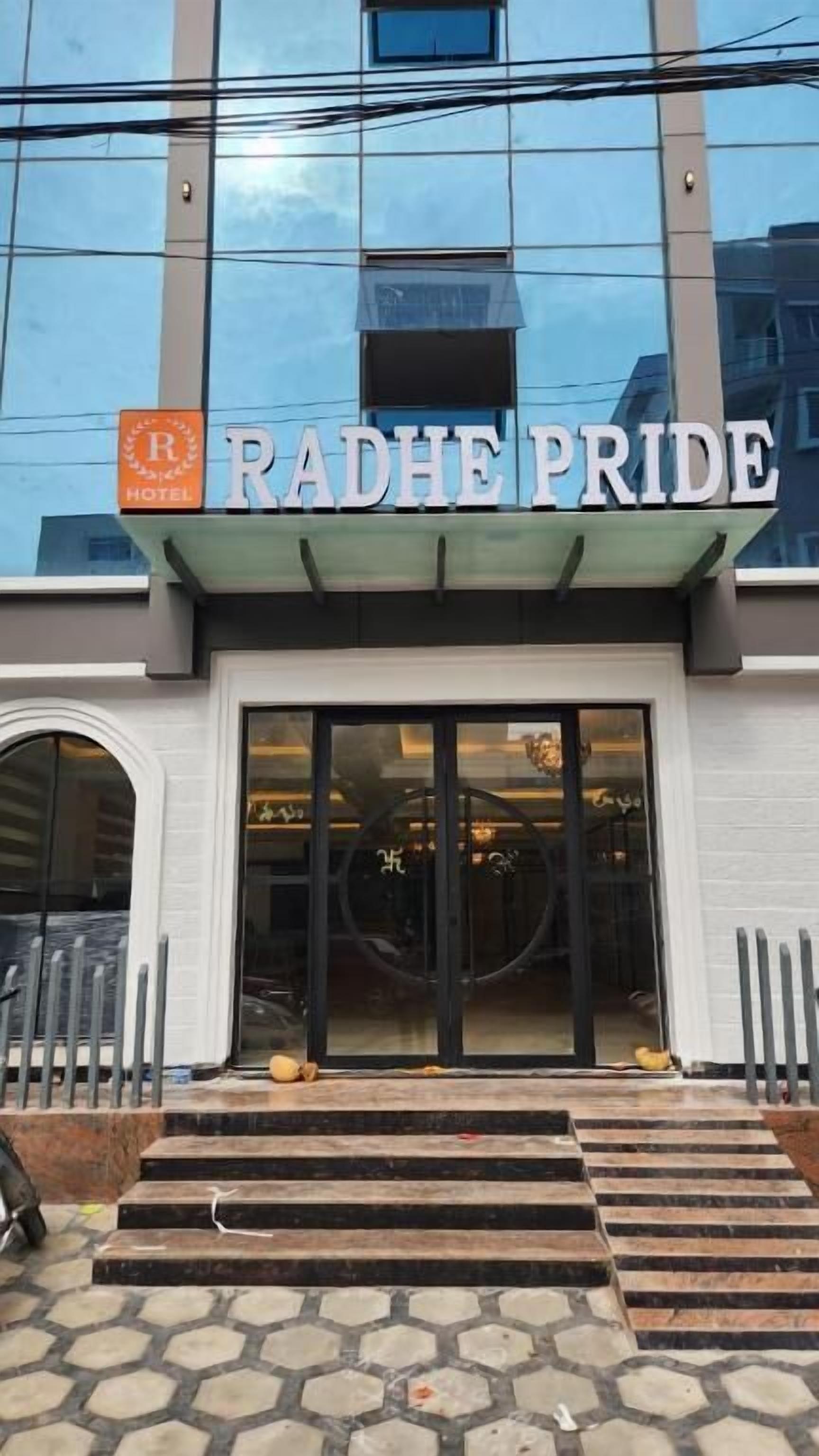 Entrada d'hotel amb façana de vidre, un cartell que diu 'RADHE PRIDE' i una rampa accessible en gades de rodes.
