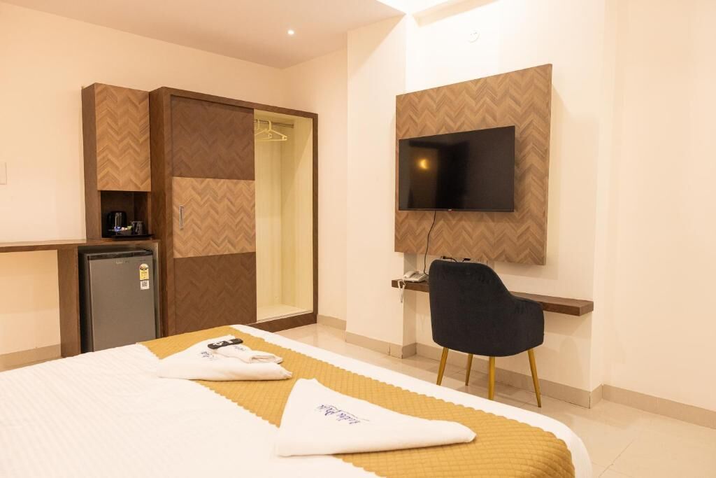 A hotel room with a bed, a desk, a television mounted on the wall, a wardrobe, and a small refrigerator.