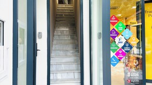 Entrada moderna de un edificio con puerta de vidrio, una escalera que conduce al interior y un anuncio amarillo a la derecha.