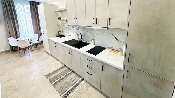 Una cocina moderna con gabinetes grises, un lavamanos negro y un salpicadero de mármol.
