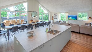 Eine moderne Küche mit einer großen Kochinsel, ein Essbereich mit Stühlen und ein Wohnzimmer mit Sofa und Fernseher.