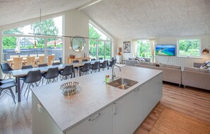 Eine moderne Küche mit einer großen Kochinsel, ein Essbereich mit Stühlen und ein Wohnzimmer mit Sofa und Fernseher.