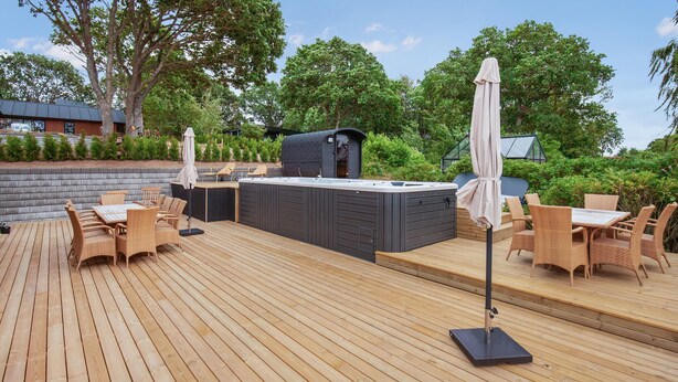 Eine Terrass mit Whirlpool, Korbmöbeln und Grill.
