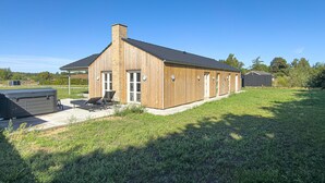 Ein Holzhaus mit geneigtem Dach, einem Schornstein und einer Terrasse mit Liegestühlen.