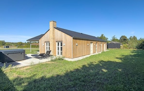 Ein Holzhaus mit geneigtem Dach, einem Schornstein und einer Terrasse mit Liegestühlen.