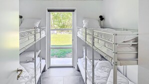 Ein schmales Zimmer mit Etagenbetten, einer Tür, die nach draußen führt, und einem Fenster mit Blick auf Grünflächen.