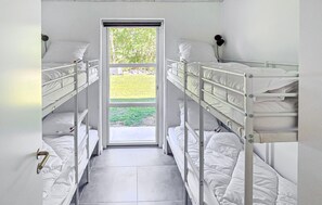 Ein schmales Zimmer mit Etagenbetten, einer Tür, die nach draußen führt, und einem Fenster mit Blick auf Grünflächen.