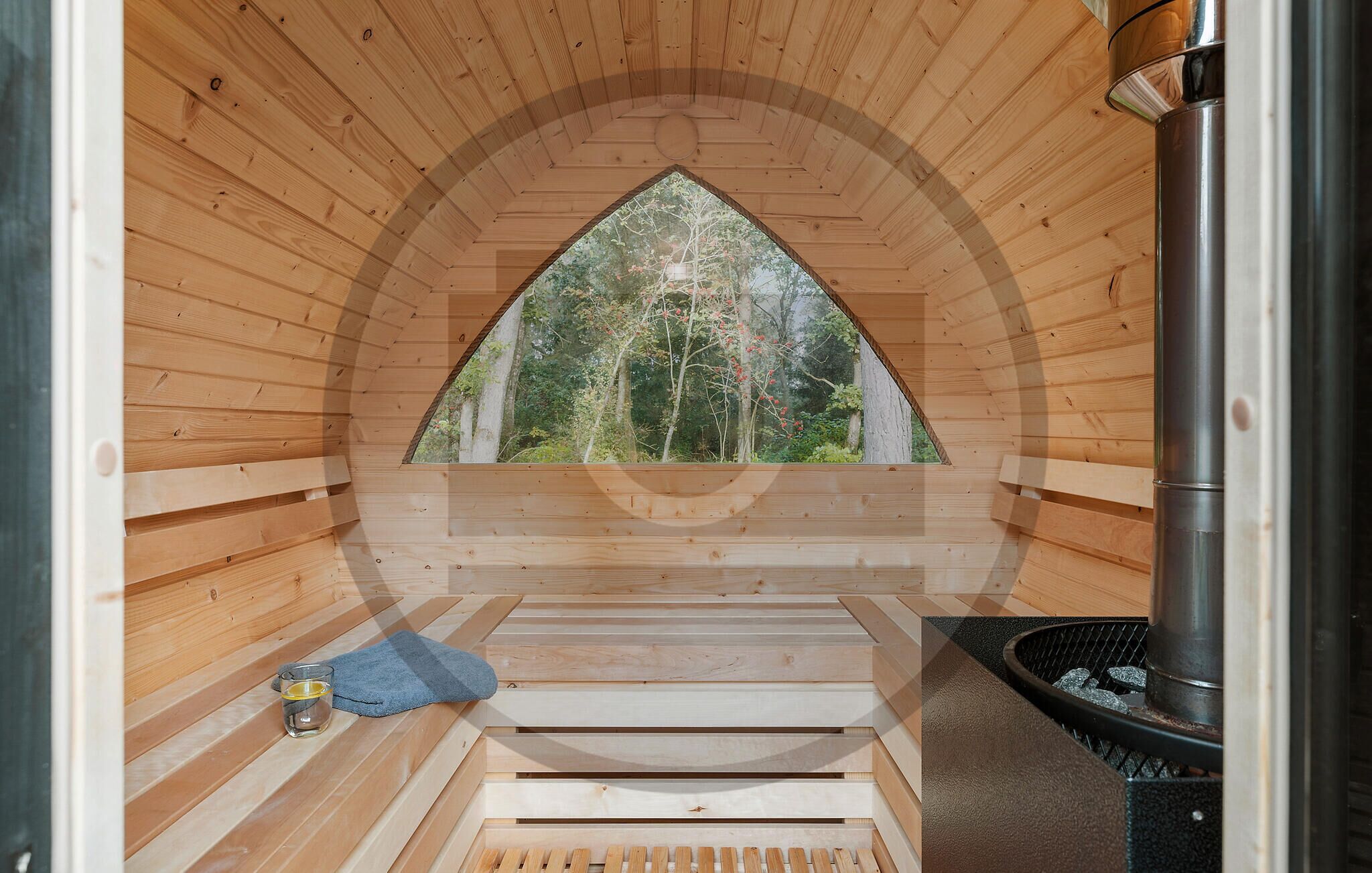 A wooden sauna with a view of a forest through a triangular window.
