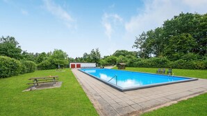 A rectangular swimming pool with a tiled deck, surrounded by a grassy area with a picnic table and benches. - Stunning home in Fårvang with sauna (Fårvang)