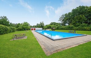 Ein rechteckiger Pool mit Fliesen umgeben, mit einer Rasenfläche, einem Picknicktisch und Bänken.