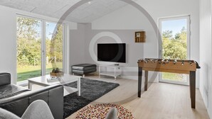A modern living room with a sofa, a coffee table, a television, and a foosball table. - Stunning home in Fårvang with sauna (Fårvang)