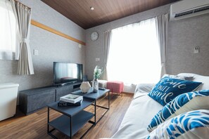 Ein modernes Hotelzimmer mit Flachbildfernseher, einem Nachttisch mit Büchern, einer dekorativen Vase und einem Bett mit blau-weißen Kissen.