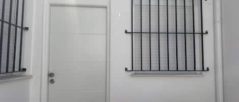 Una puerta blanca con una reja de metal, una ventana con barrotes y un banco.