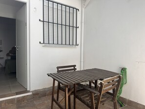 Um pátio com mesa e cadeiras de madeira, uma janela com grades e uma mangueira de jardim verde.