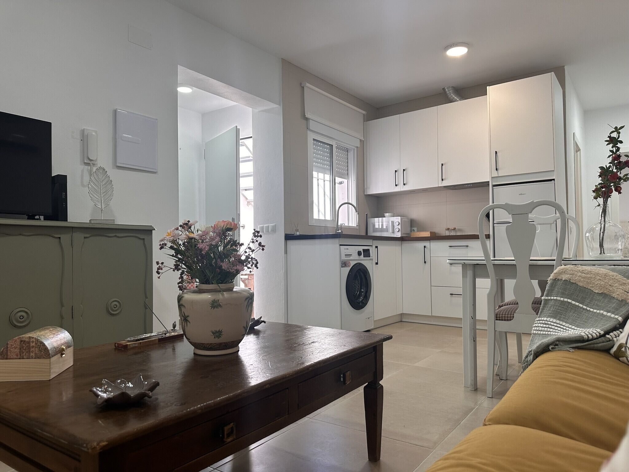 Una cuina moderna amb armaris blancs, rentadora i zona de menjador amb taula i cadires.