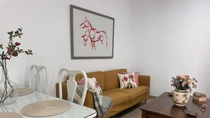 Ett vardagsrum med ett matbord i glas, en brun soffa, ett soffbord i trä och en inramad abstrakt målning.