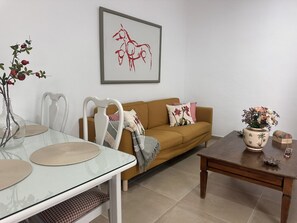 Ein Wohnzimmer mit einem Glastisch, einem braunen Sofa, einem Couchtisch aus Holz und einem gerahmten abstrakten Gemälde.