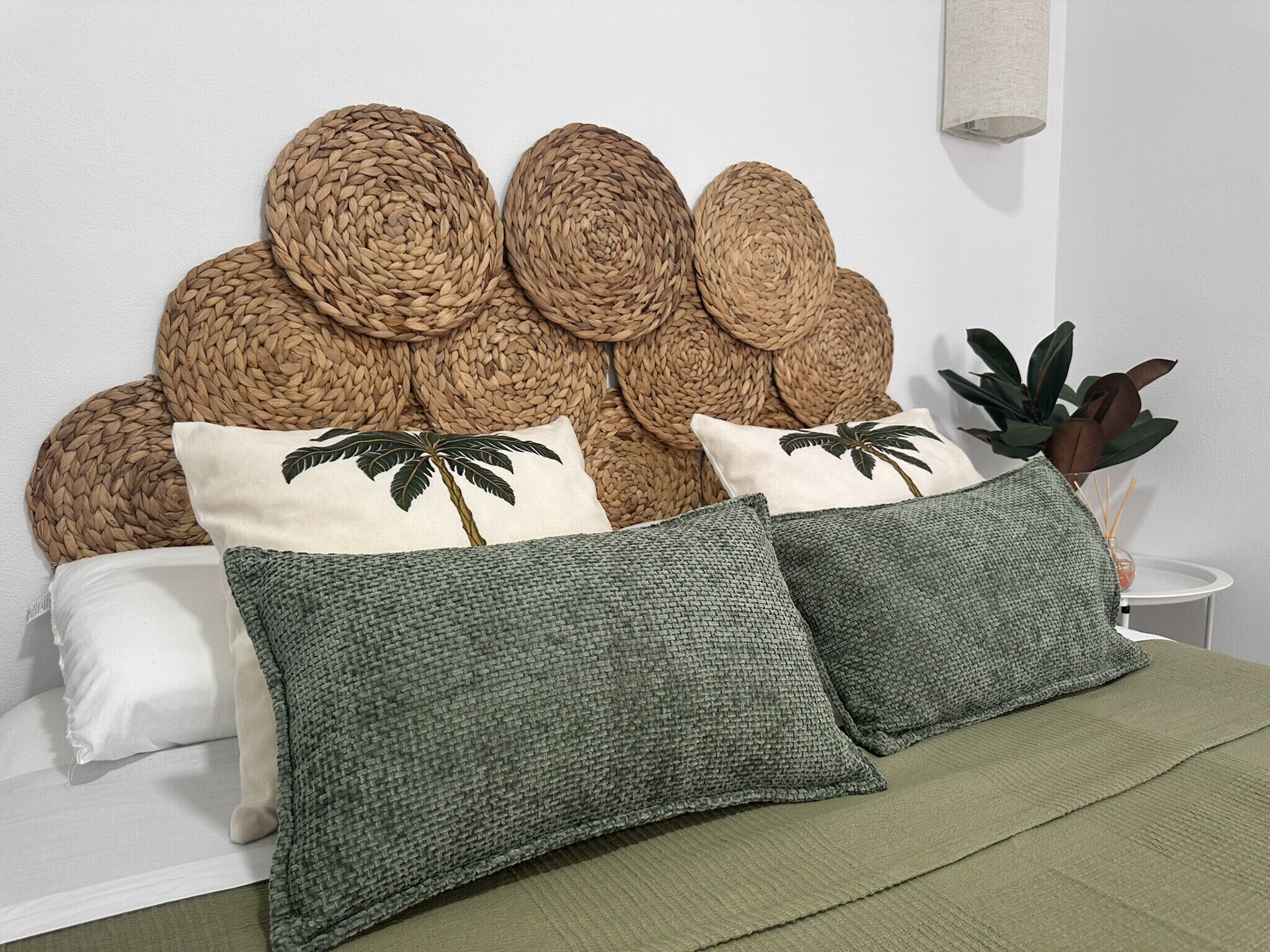 A bed with a woven headboard, two pillows with palm tree designs, and a green blanket.