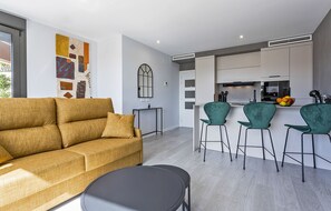 A modern living room with a sofa, a round table, and a kitchen area with a bar. - Sky Garden Jerez - Ole Solutions (Jerez de la Frontera)