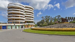 A multi-story hotel with balconies, a parking area, and a landscaped area with a sculpture. - Sky Garden Jerez - Ole Solutions (Jerez de la Frontera)