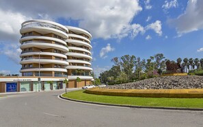 A multi-story hotel with balconies, a parking area, and a landscaped area with a sculpture. - Sky Garden Jerez - Ole Solutions (Jerez de la Frontera)