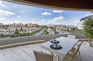 Ein Balkon mit Tisch und Stühlen, einem Blumentopf und Blick auf eine Stadtlandschaft.