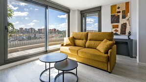 A modern living room with a sofa, two small tables, a fireplace, and large windows offering a city view. - Sky Garden Jerez - Ole Solutions (Jerez de la Frontera)