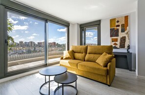 A modern living room with a sofa, two small tables, a fireplace, and large windows offering a city view. - Sky Garden Jerez - Ole Solutions (Jerez de la Frontera)